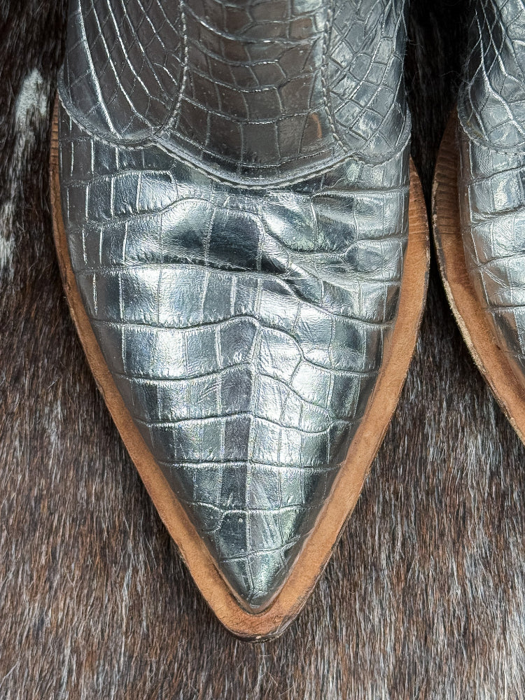 Close-up of silver crocodile skin boots on a textured surface